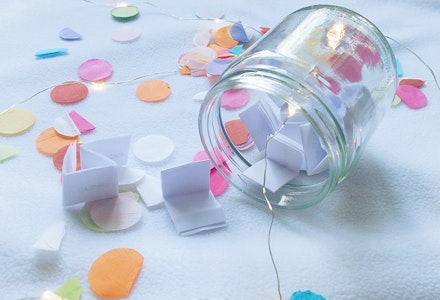 Glass wish jar filled with paper wishes on a table with confetti
