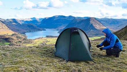 one-person-tent Hiker pitching a one-person tent on a hilltop