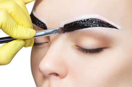 The make-up artist applies a paints eyebrow dye on the eyebrows of a young girl. Professional face care. The make-up artist applies a paints eyebrow dye on the eyebrows of a young girl. Professional face care.
