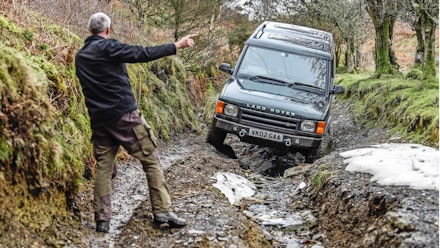 Land Rover Discovery being guided over a washed-out section of greenlane Land Rover Discovery being guided over a washed-out section of greenlane