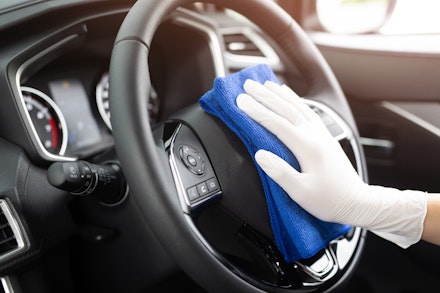 A hand cleans a car's steering wheel using a drying towel A hand cleans a car's steering wheel using a drying towel