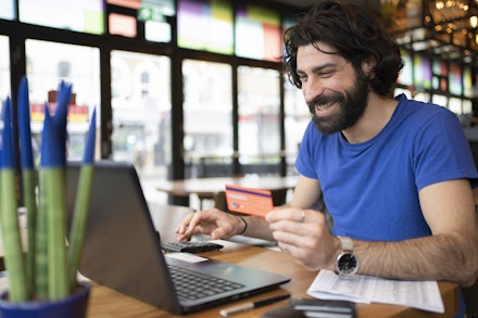 A man holds a card as he buys something on a laptop A man holds a card as he buys something on a laptop