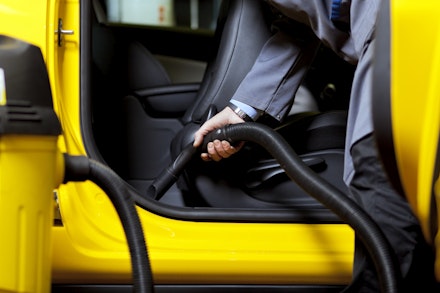 A person vacuuming the seats of a yellow car A person vacuuming the seats of a yellow car