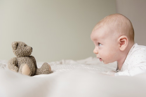Caucasian baby staring at teddy bear on bed Week 8