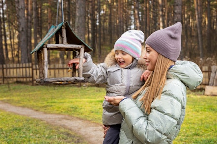 Family at autumn park. Young mother shows her daughter bird feeder outside. mum and child feeding birds