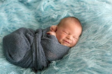 Happy smiling newborn baby in wrap, sleeping happily in cozy blue fur, cute infant baby smiling newborn in swaddle