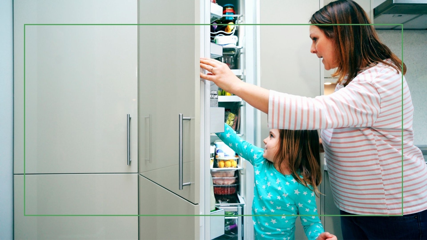 Mum and daughter opening integrated fridge freezer door Getty