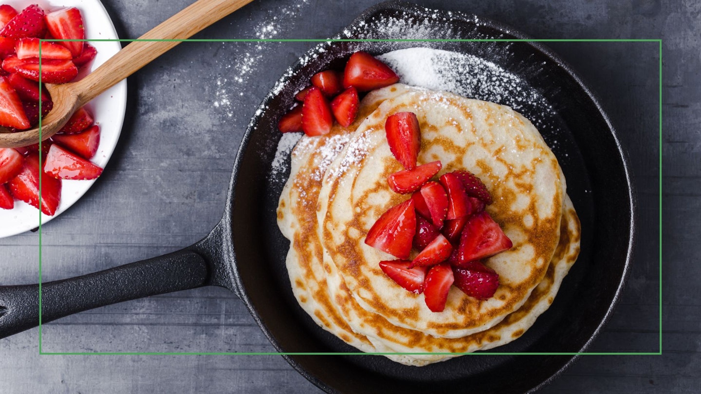 Breakfast or brunch, favourite morning meal. Homemade berry pancakes in cast iron skillet, fresh summer dessert with strawberries viewed from above