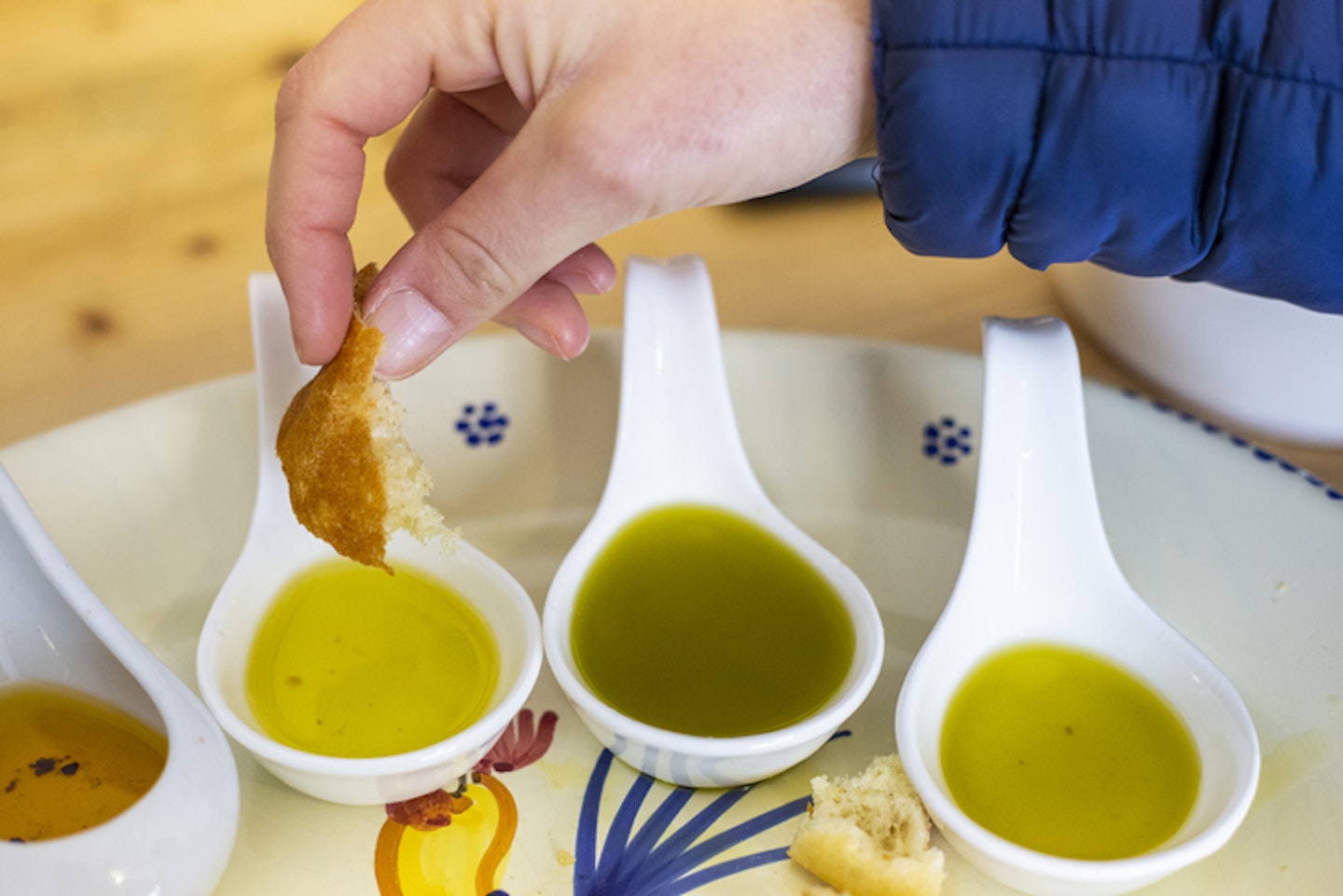 A human hand dips bread in different types of flavored extra virgin olive oils from Apulia, Italy.