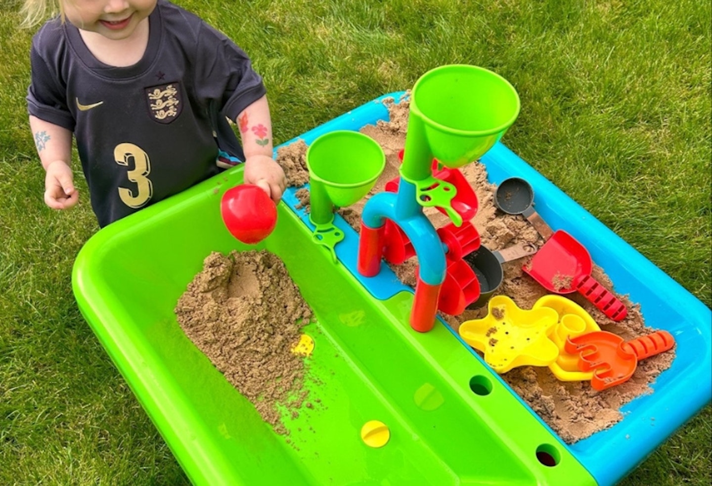 child playing with the Early Learning Centre Sand and Water Table, putting some of the sand into the empty side of the table