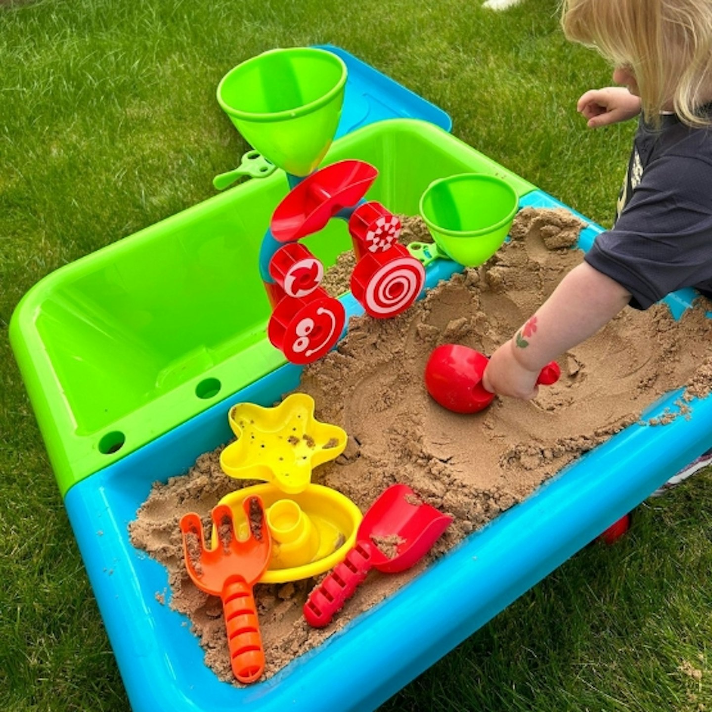 Child playing with the Early Learning Centre Sand and Water Table, putting some of the sand into the empty side of the table