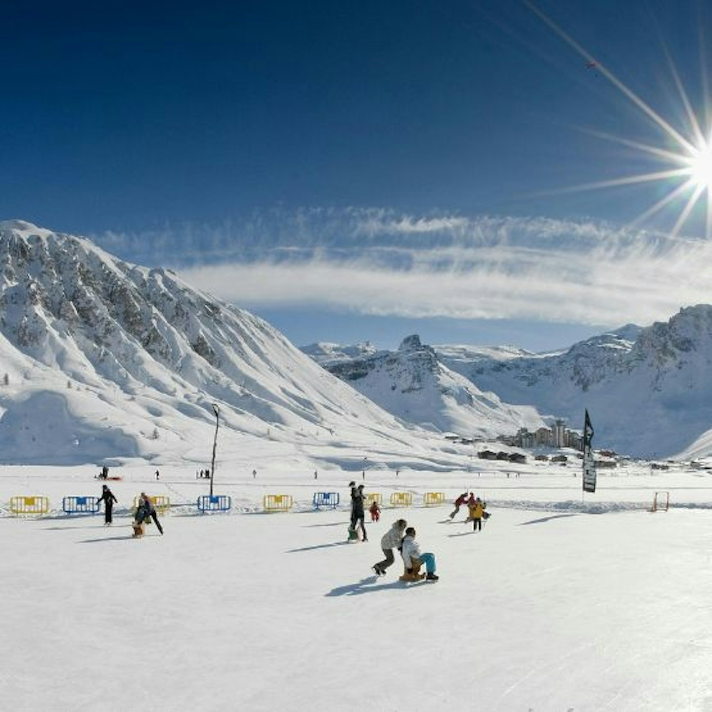 Skiers on the snow at Tignes with ski slopes beyond and blue sky