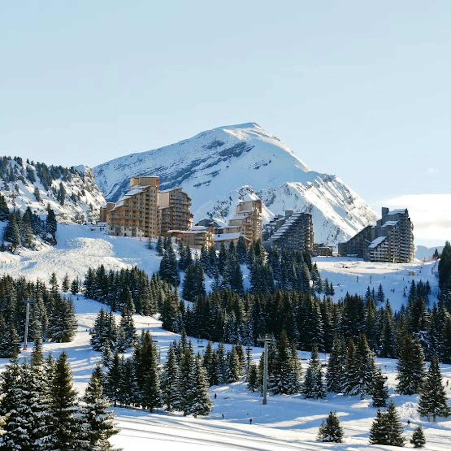 Snowy mountains with buildings in the distance and fir tress around
