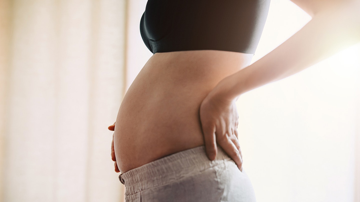 Side profile, mid-section of pregnant woman gently touching her belly
