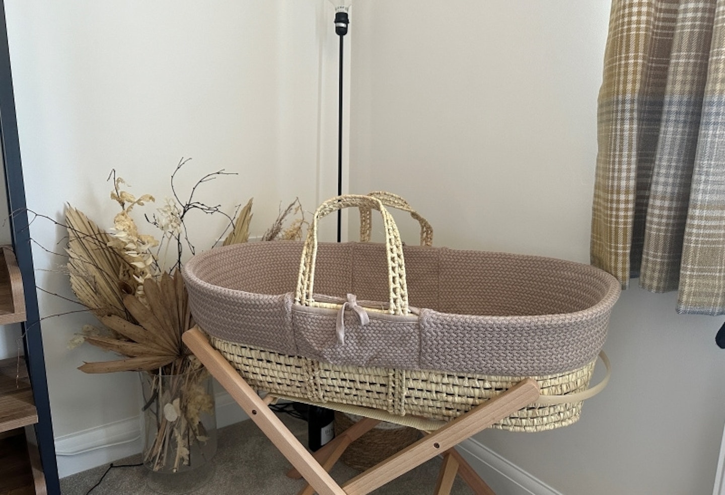 The Little Green Sheep Natural Knitted Moses Basket & Mattress on stand in the corner of a room