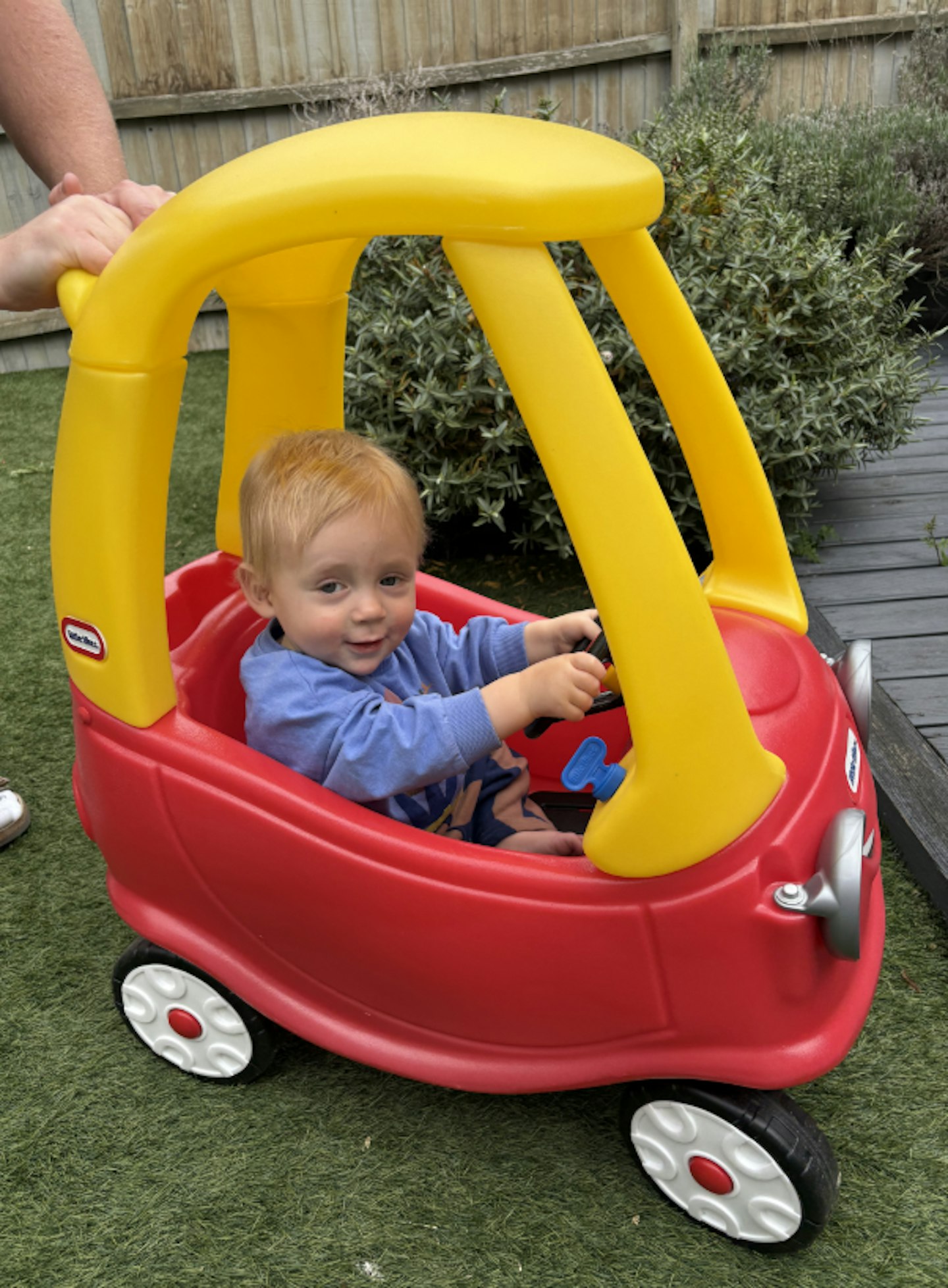 A one year old sitting in a red and yellow Little Tikes Cozy Coupe