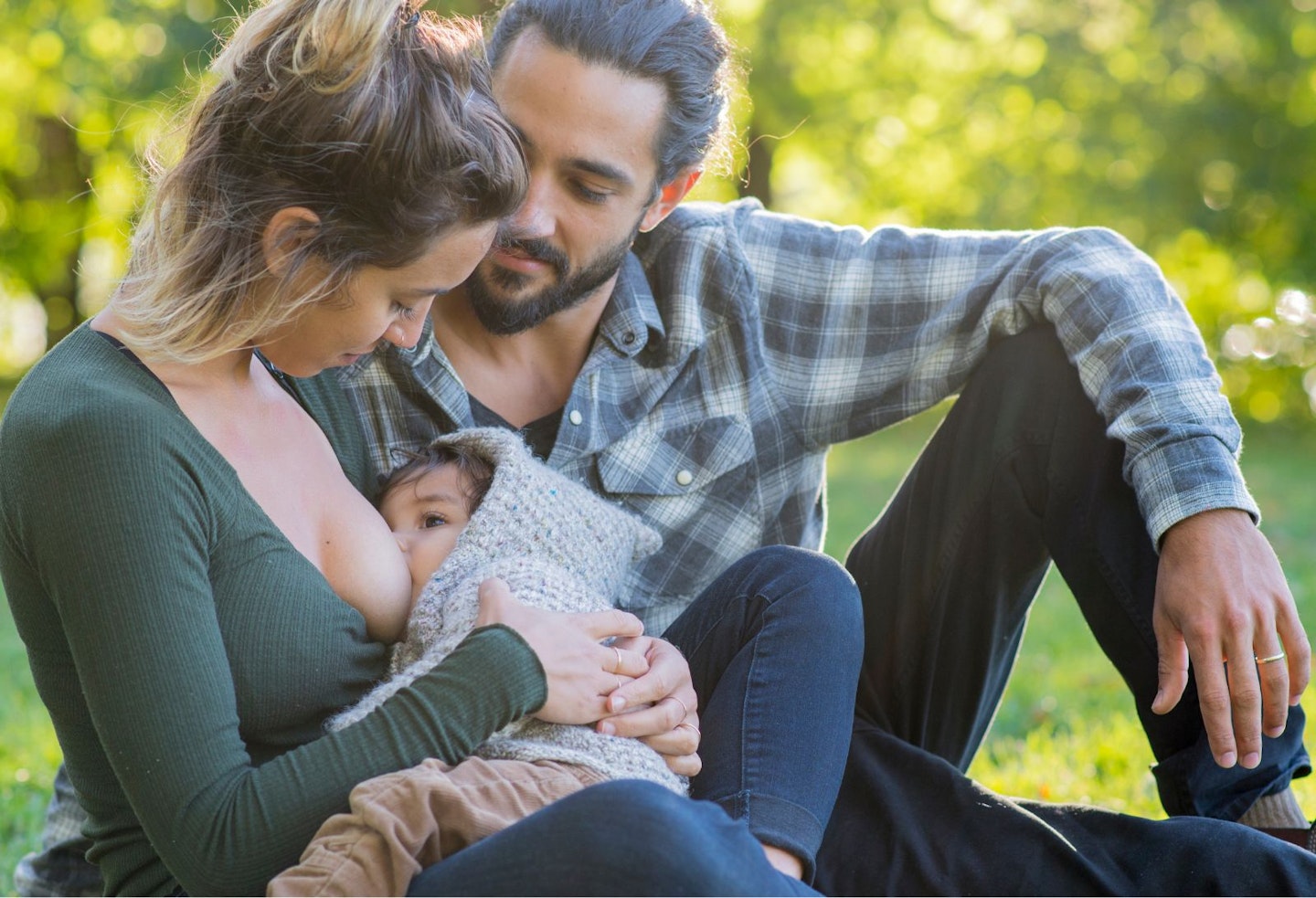 Young family in the park, mother breastfeeding in public with her husband