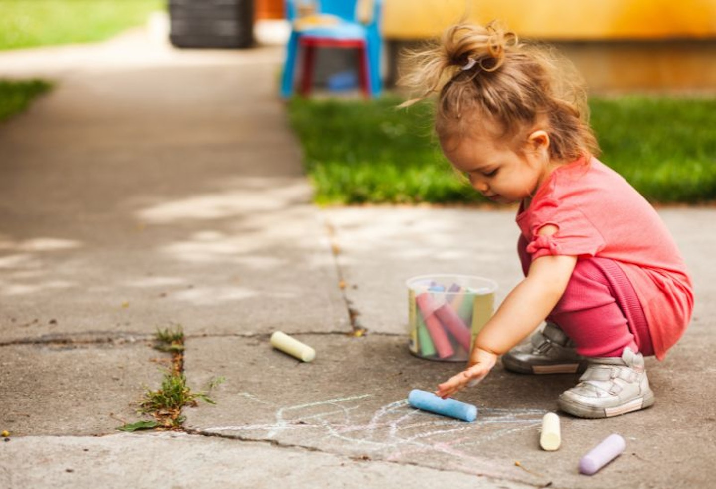 Toddler kneeling and chalk drawing on the flagstones with giant chalk pieces