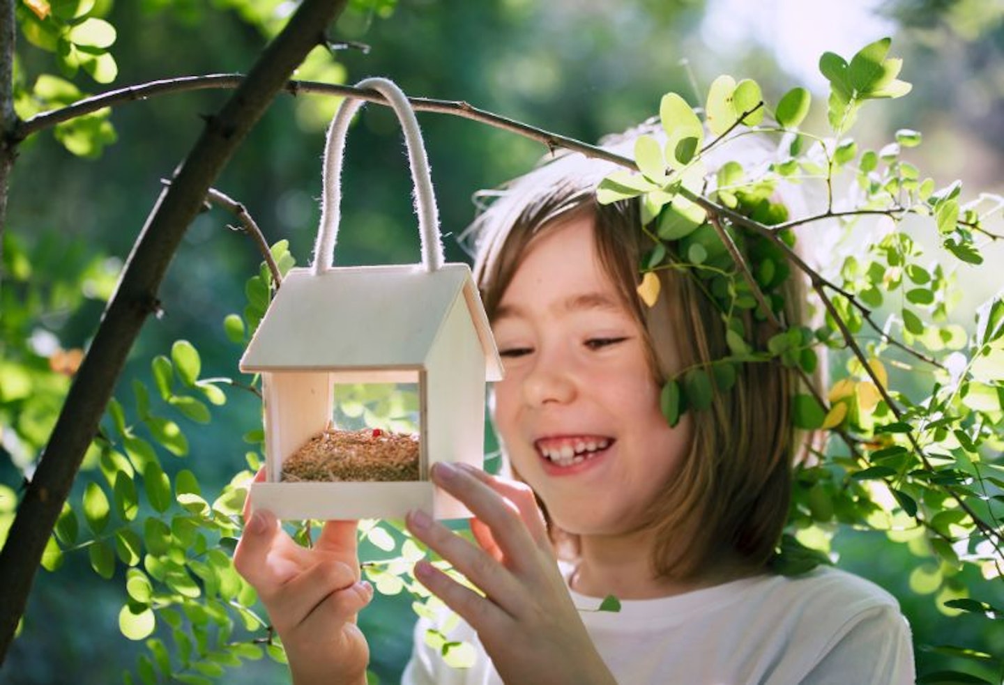 Smiling child checking a bird feeder hanging from a tree branch in the garden