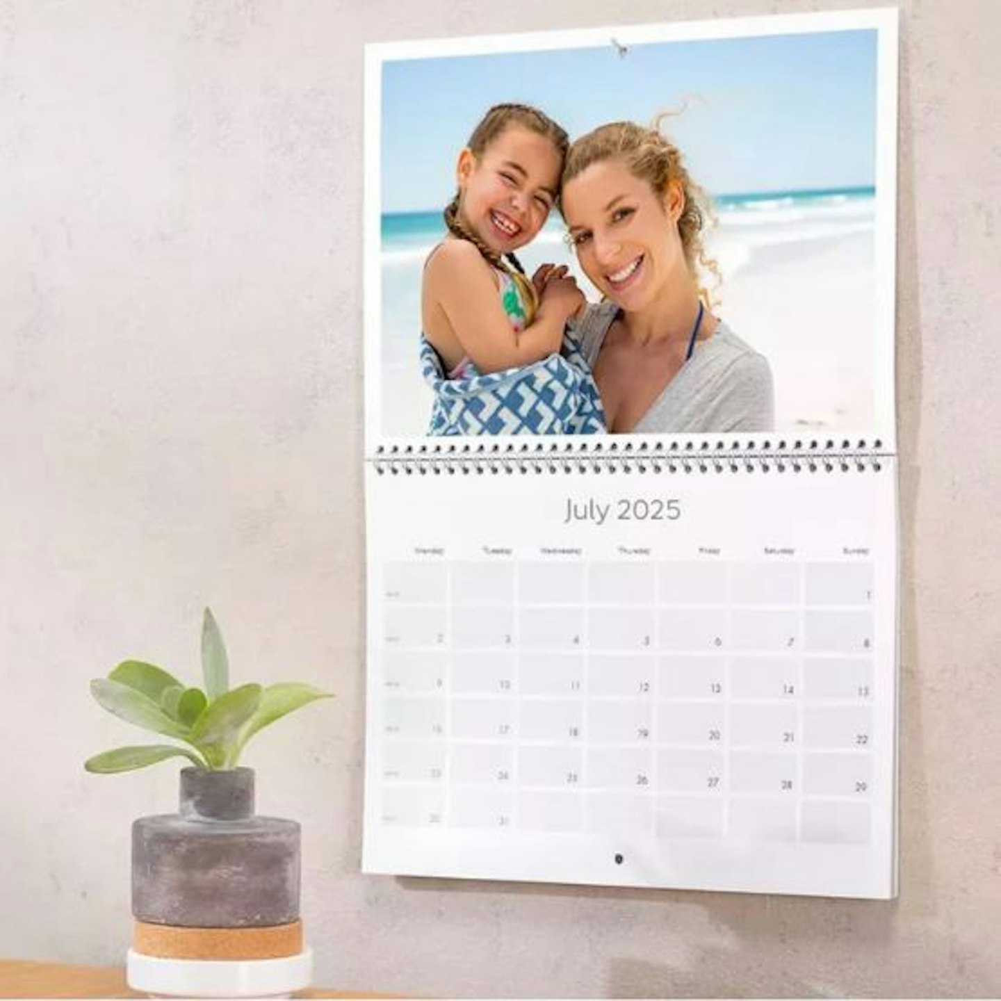 A personalised photo calendar hanging on a wall with a pot plant in front