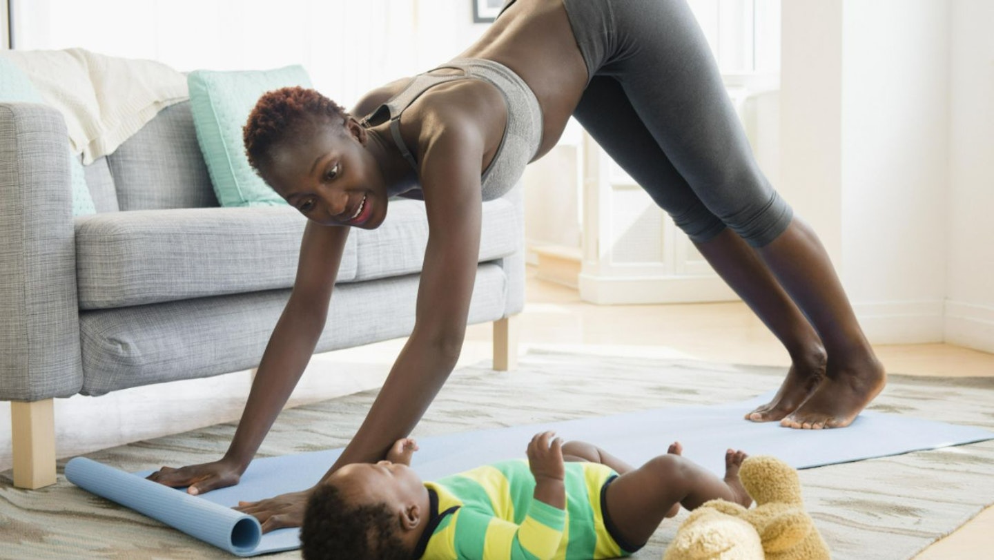 Black mum working out with baby lying on floor