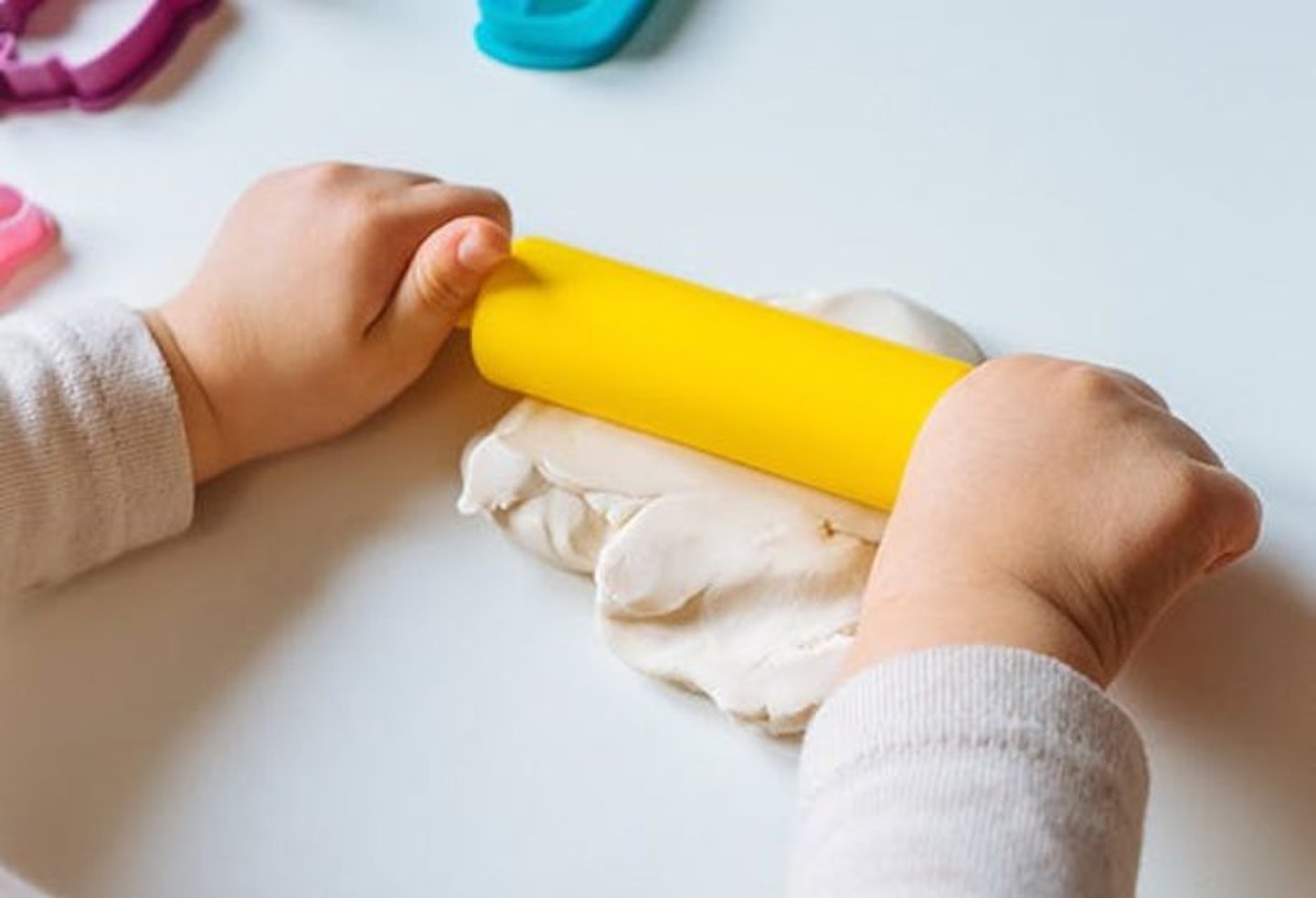 A child's hands rolling out play doh with a yellow rolling pin as an activity for one year olds