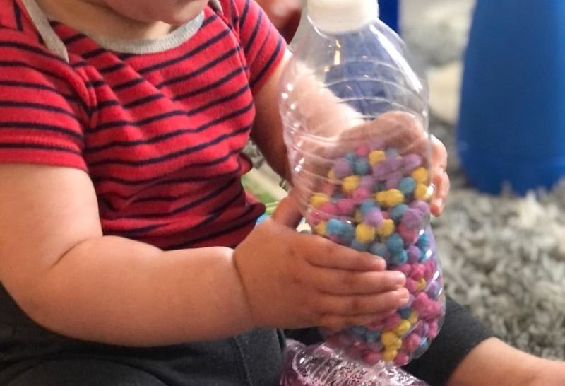 A baby sitting with a plastic bottle of small colourful beads as a shaker