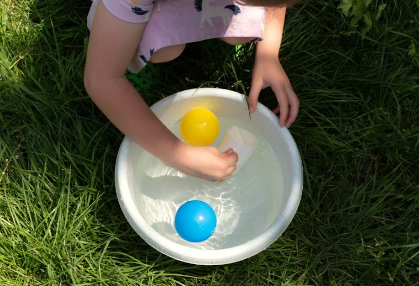 A child playing with balls in a bowl of water in the garden