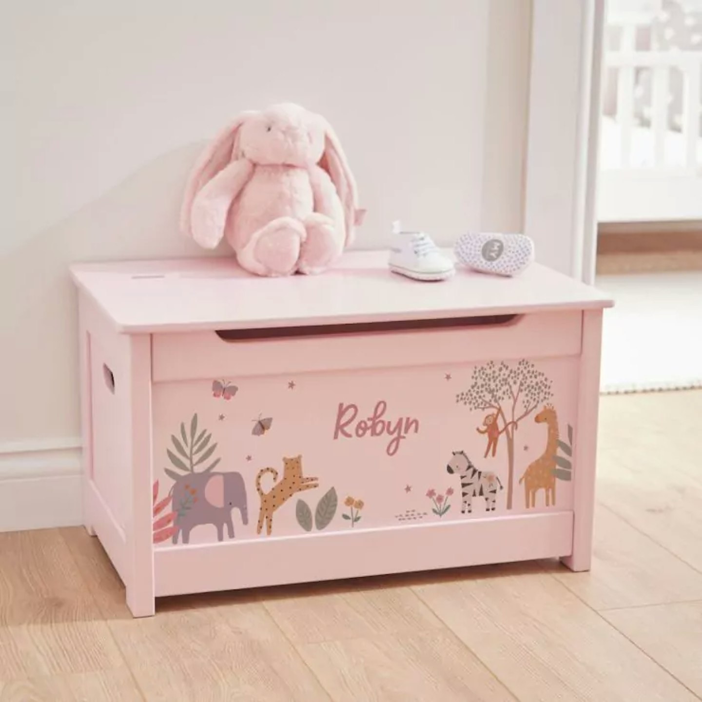 lifestyle shot of a pink storage toy box with a cuddly bunny rabbit sitting on top of it.