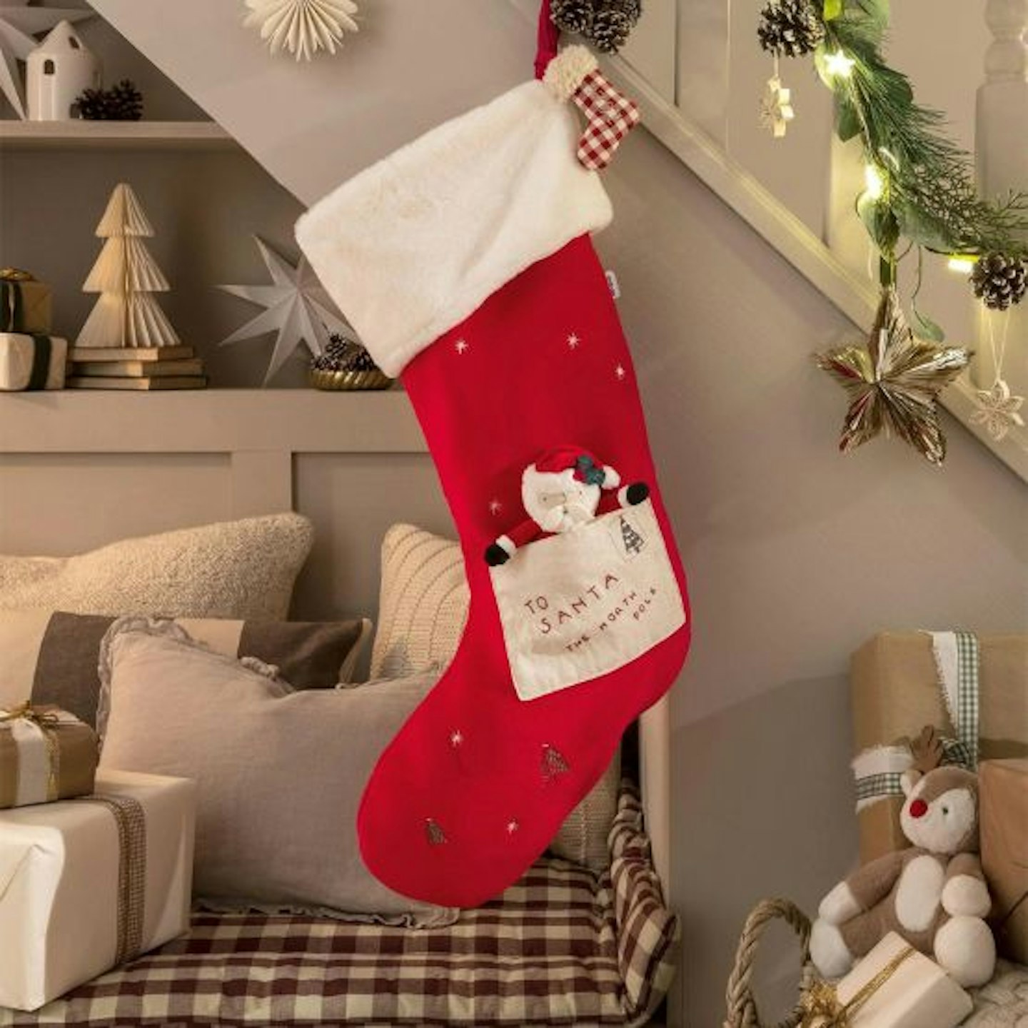 A staircase with a large Christmas stocking hung on the side in red with a white trim and a little Santa toy in an envelope on the side