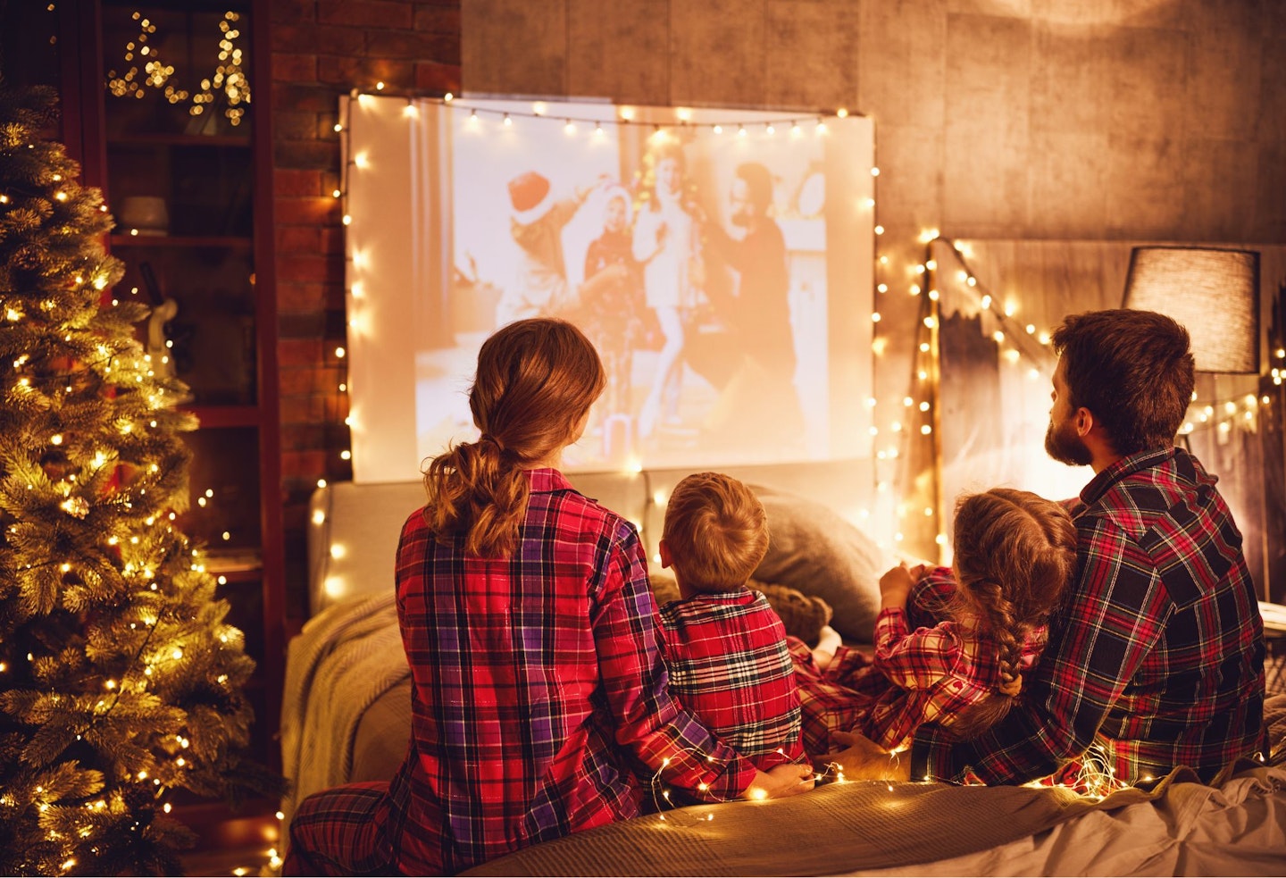 A family in matching Christmas pyjamas watching a film 