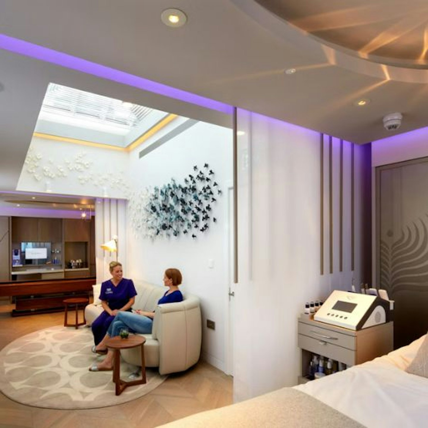 A therapy room showing two women talking, a massage bed and a machine