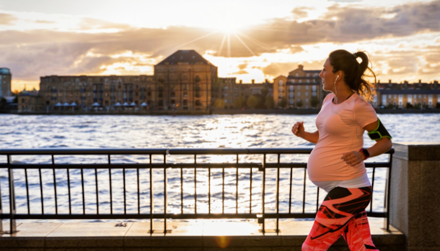 Pregnant woman running outside in a city at the riverside