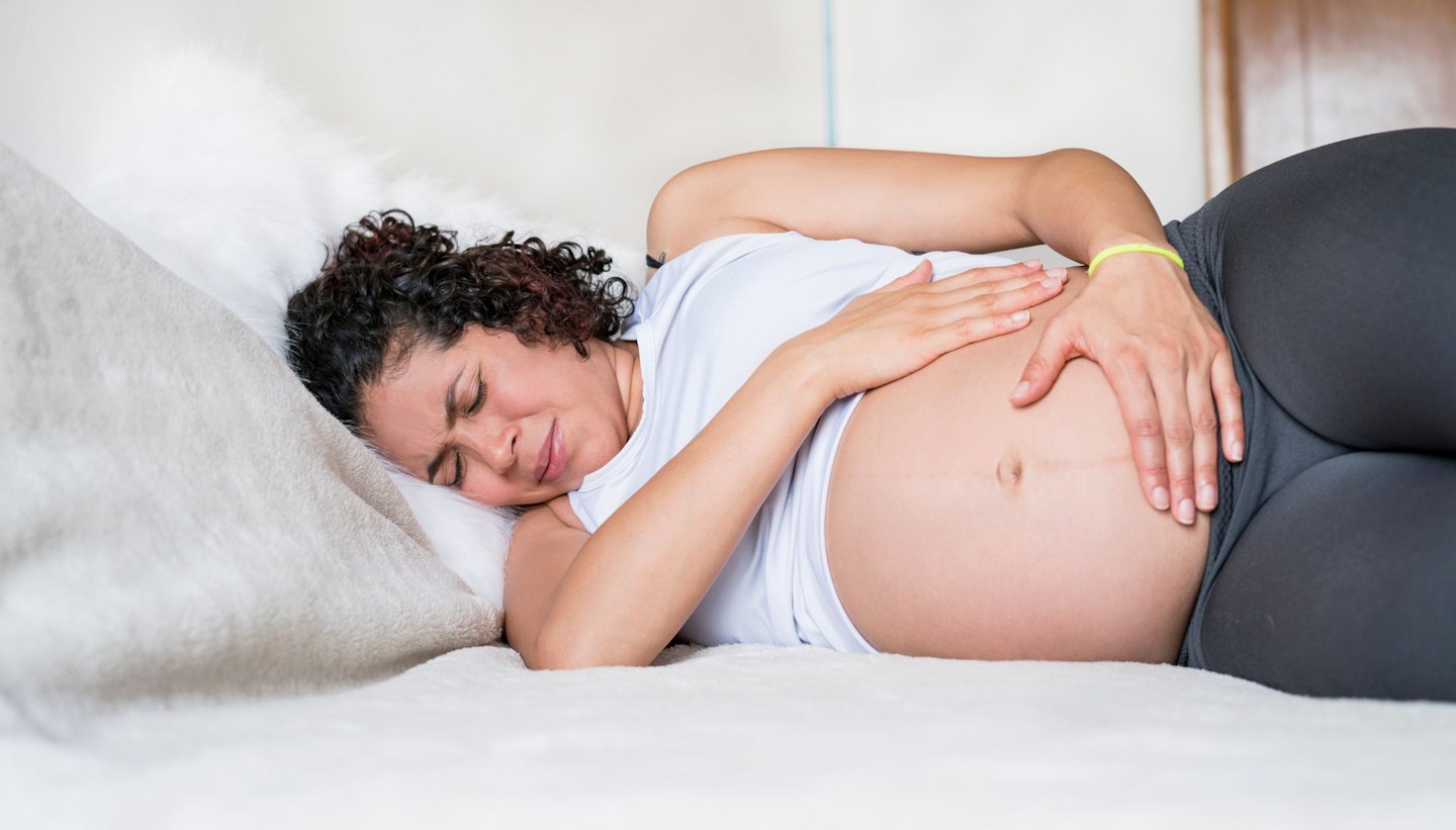Pregnant ethnic latin woman lying on a bed with pelvic pains touching her belly.