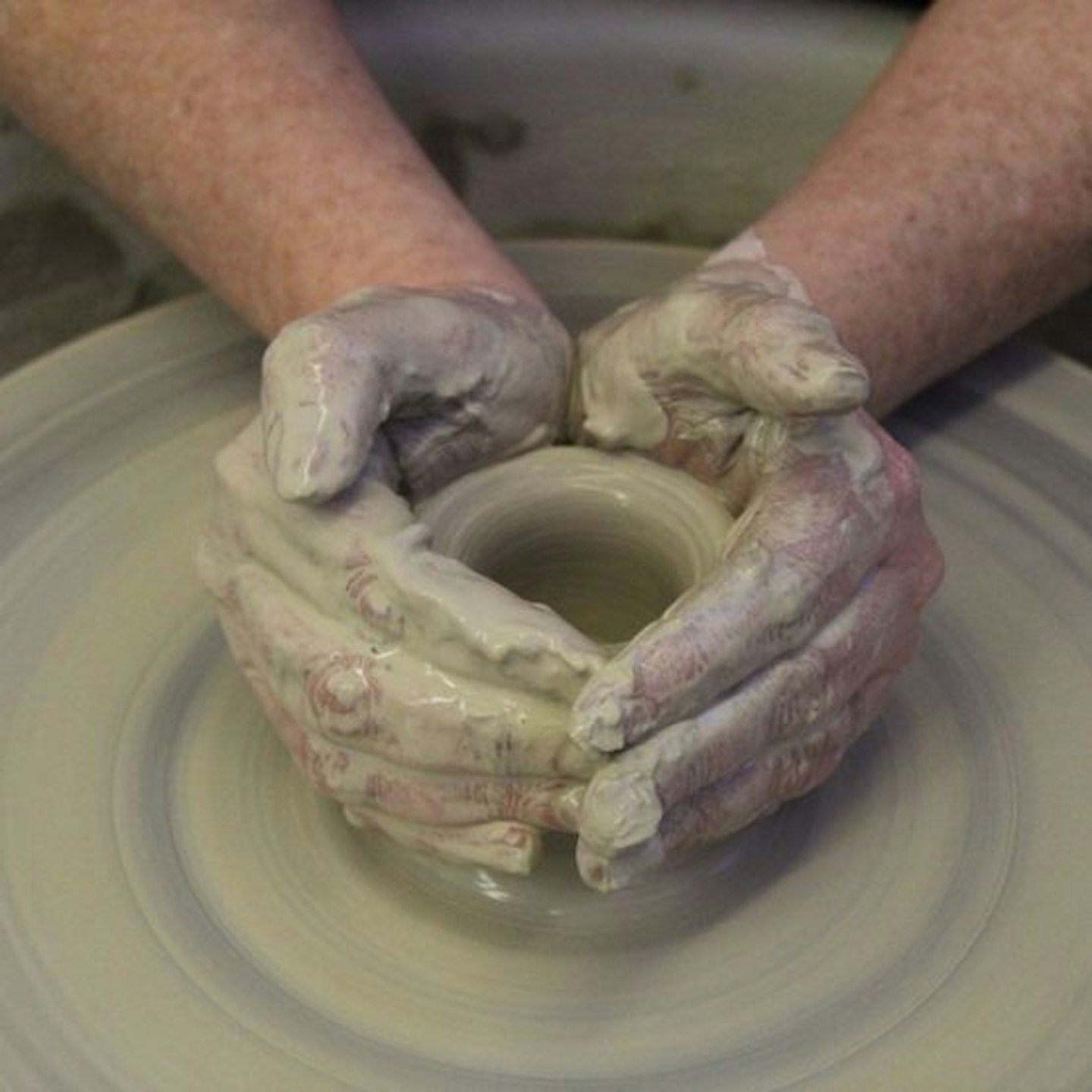 A potter holding a pot on the wheel with clay on their hands