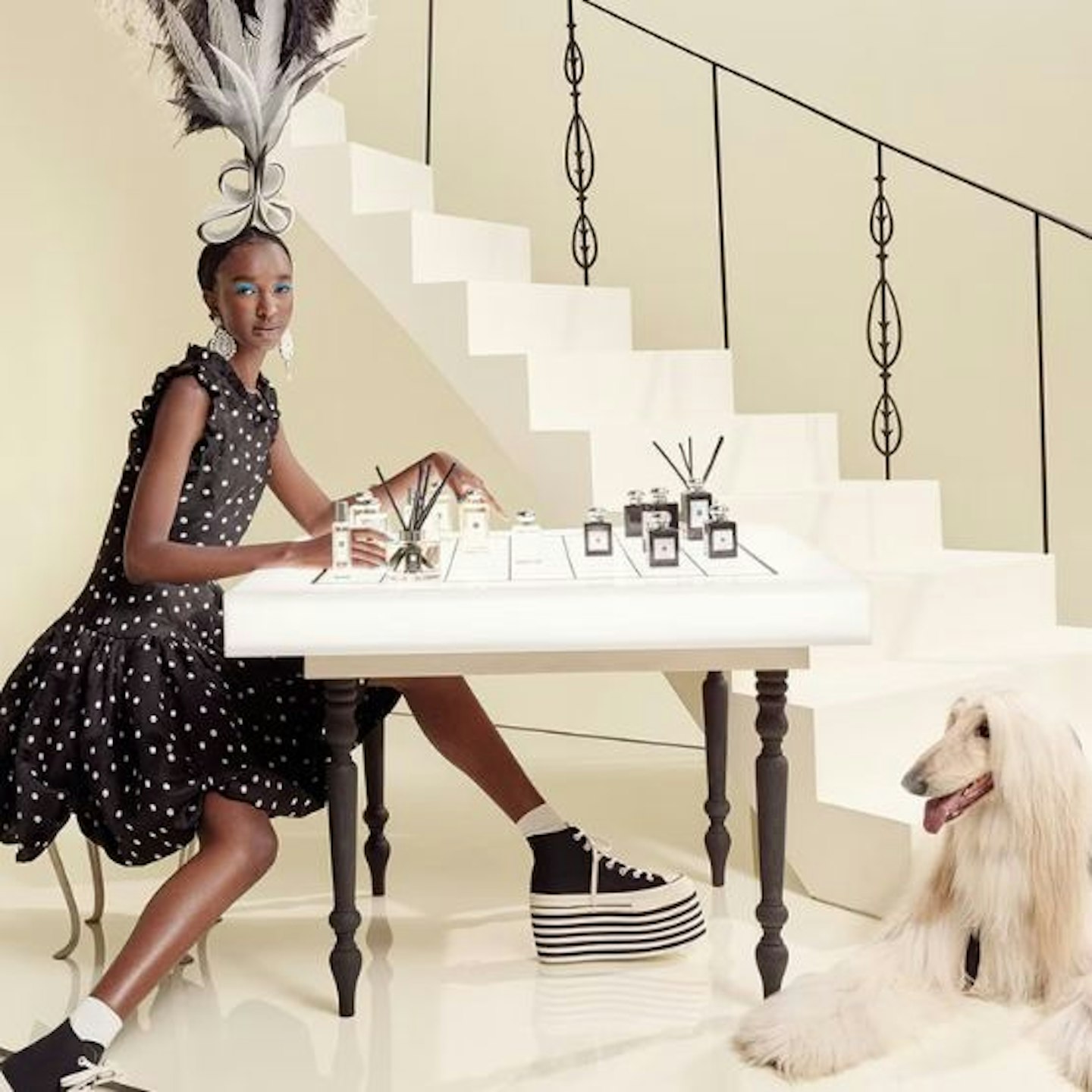 A model in a black dress sitting at a table with a long haired white puddle next to her 