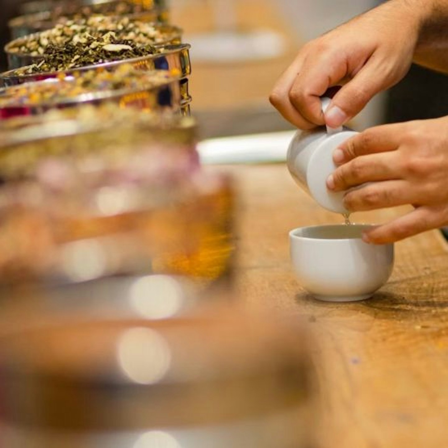 A selection of jars with different tea leaves in and a pair of hands pouring water into a pot