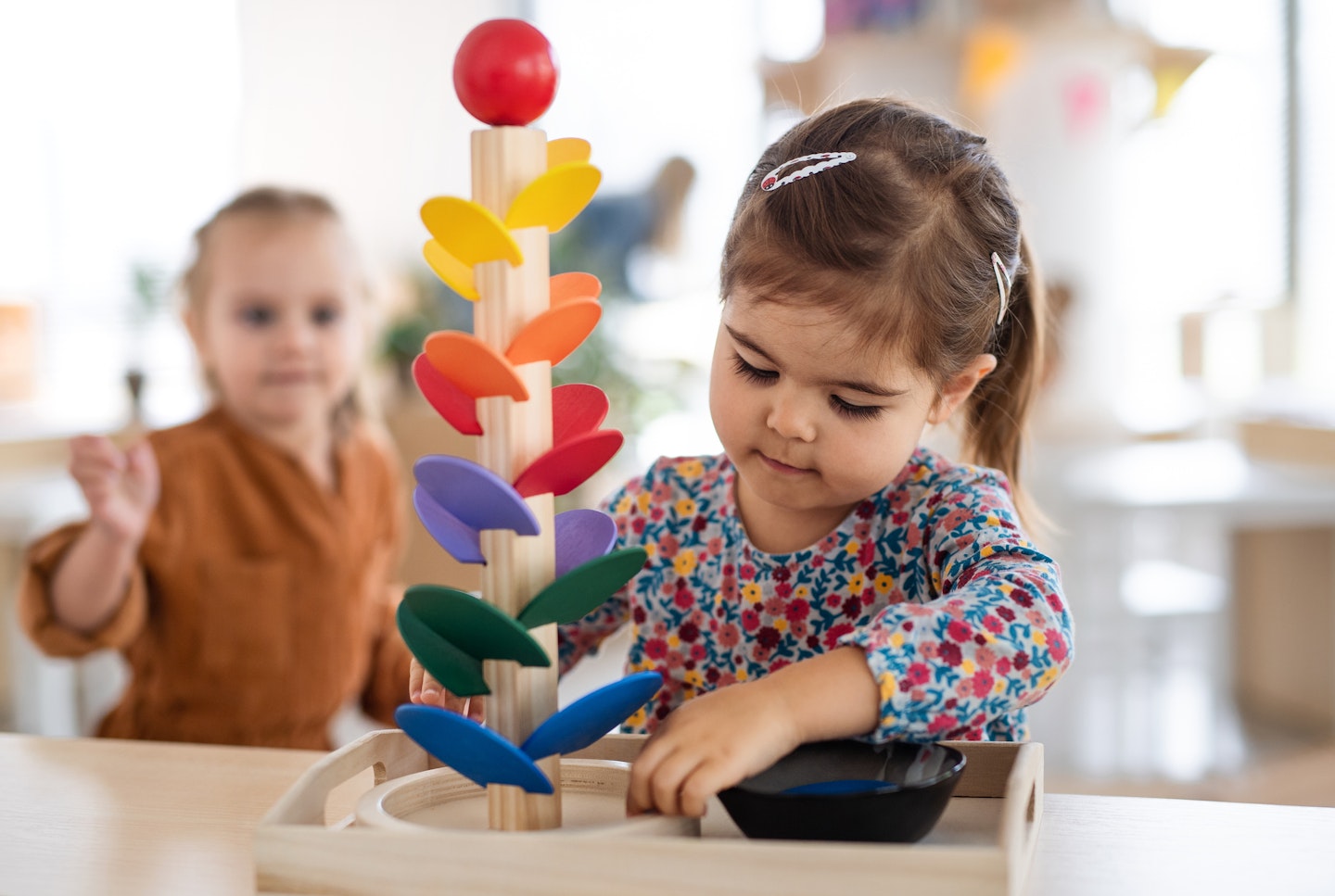Two pre-school girls playing with marble run indoors in nursery, Montessori education.