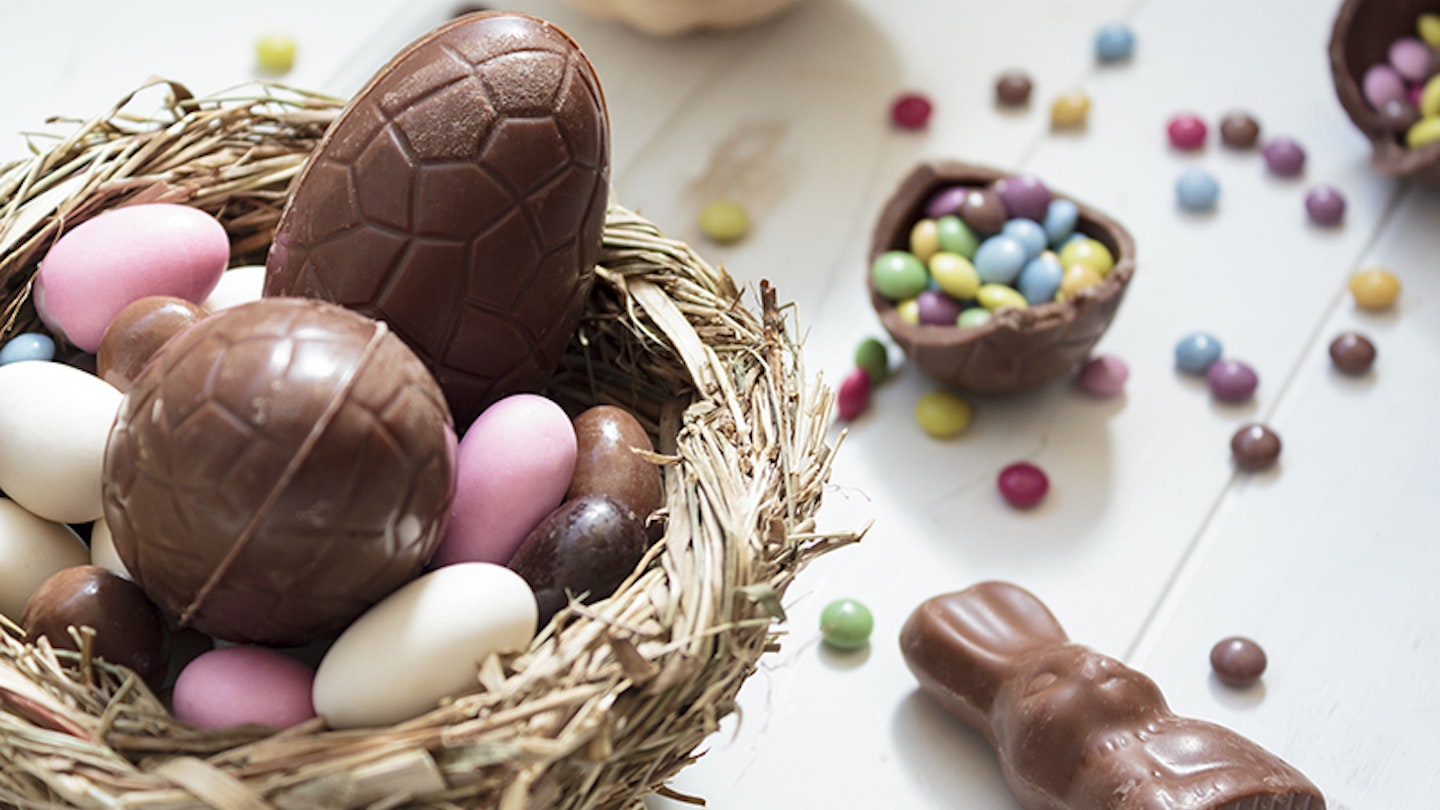 Chocolate eggs and easter almonds on bird nest, chocolate bunny and sweets on white wooden table