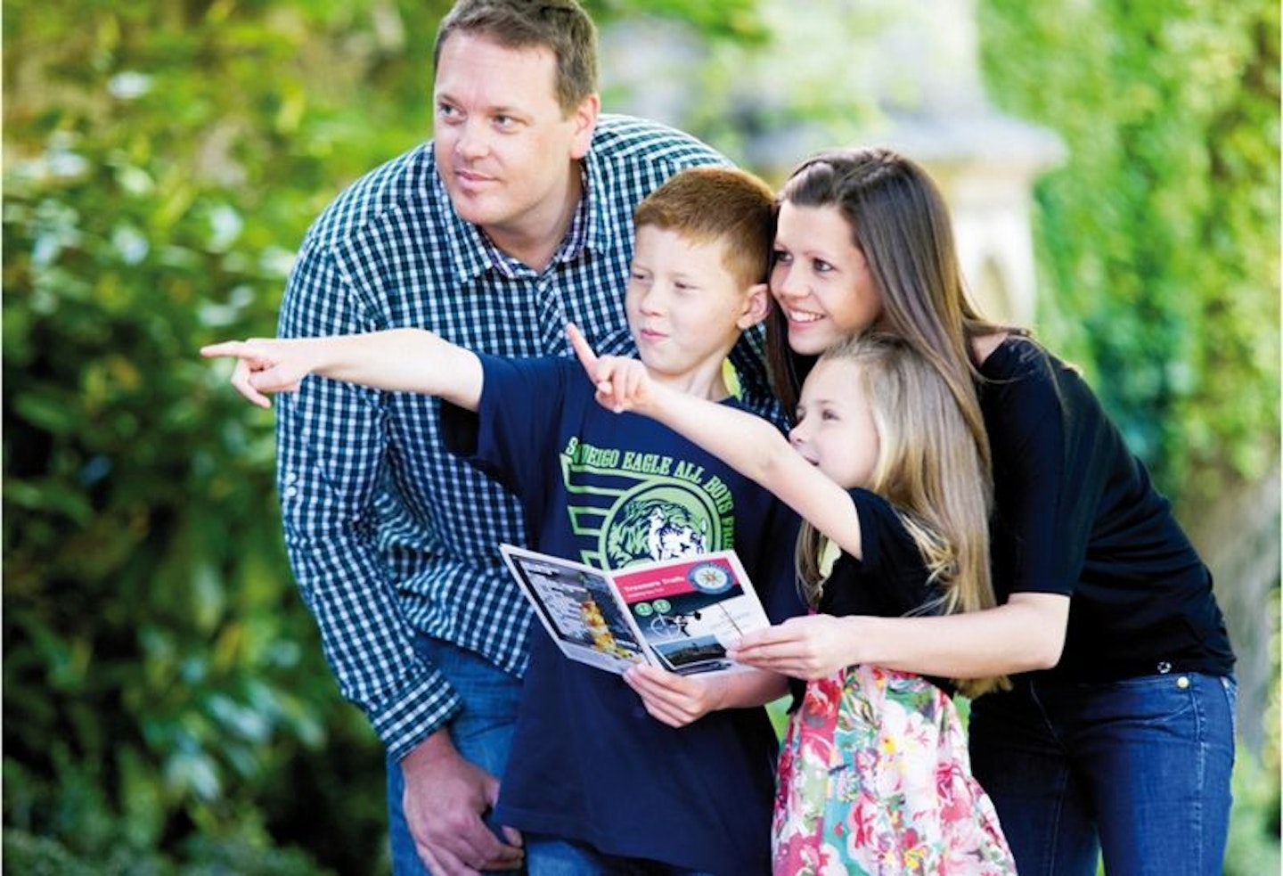 A family of four holding a treasure map and pointing into the distance