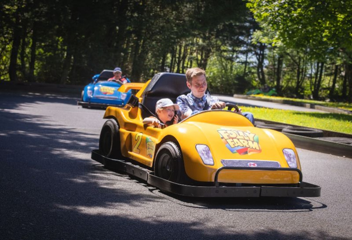 A man and his son driving a yellow toy car at Folly Farm, Wales