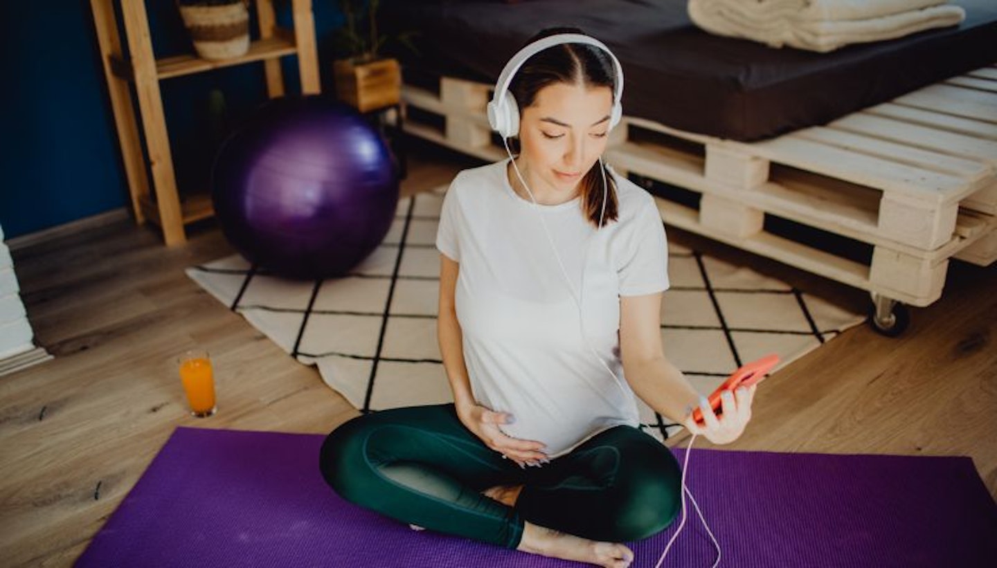 Woman sitting on yoga mat listening to music or audiobook with headphones