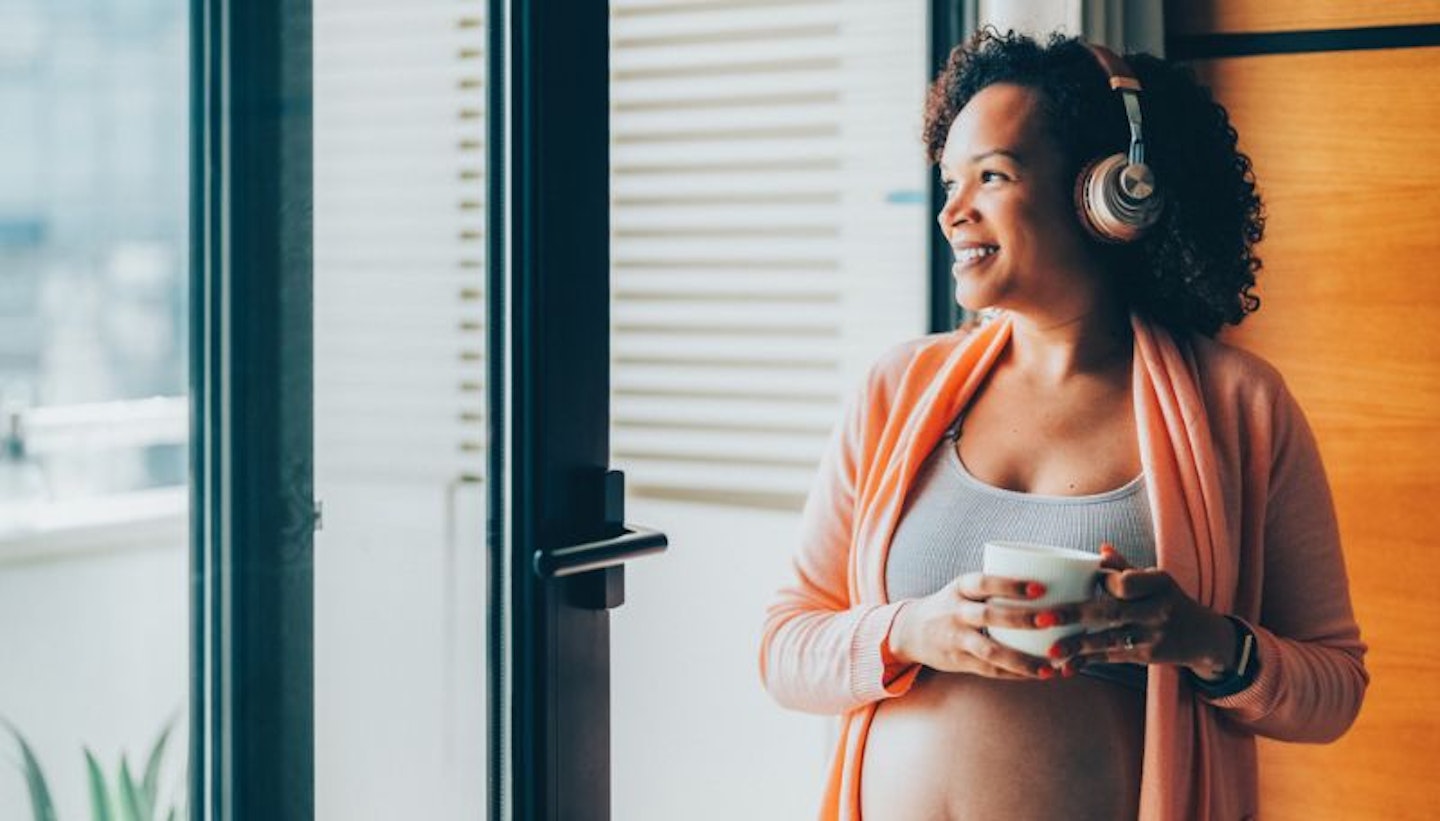 Woman looking out of window smiling and listening to audiobook on headphones