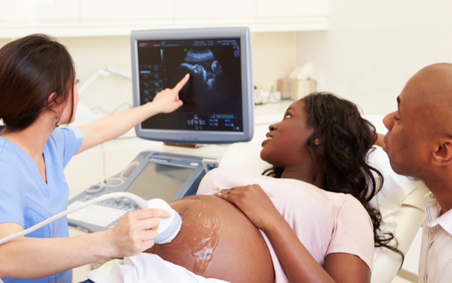 Pregnant Woman And Partner Having 4D Ultrasound Scan, Pregnant Woman And Partner Having Ultrasound Scan With Nurse Pointing To Screen