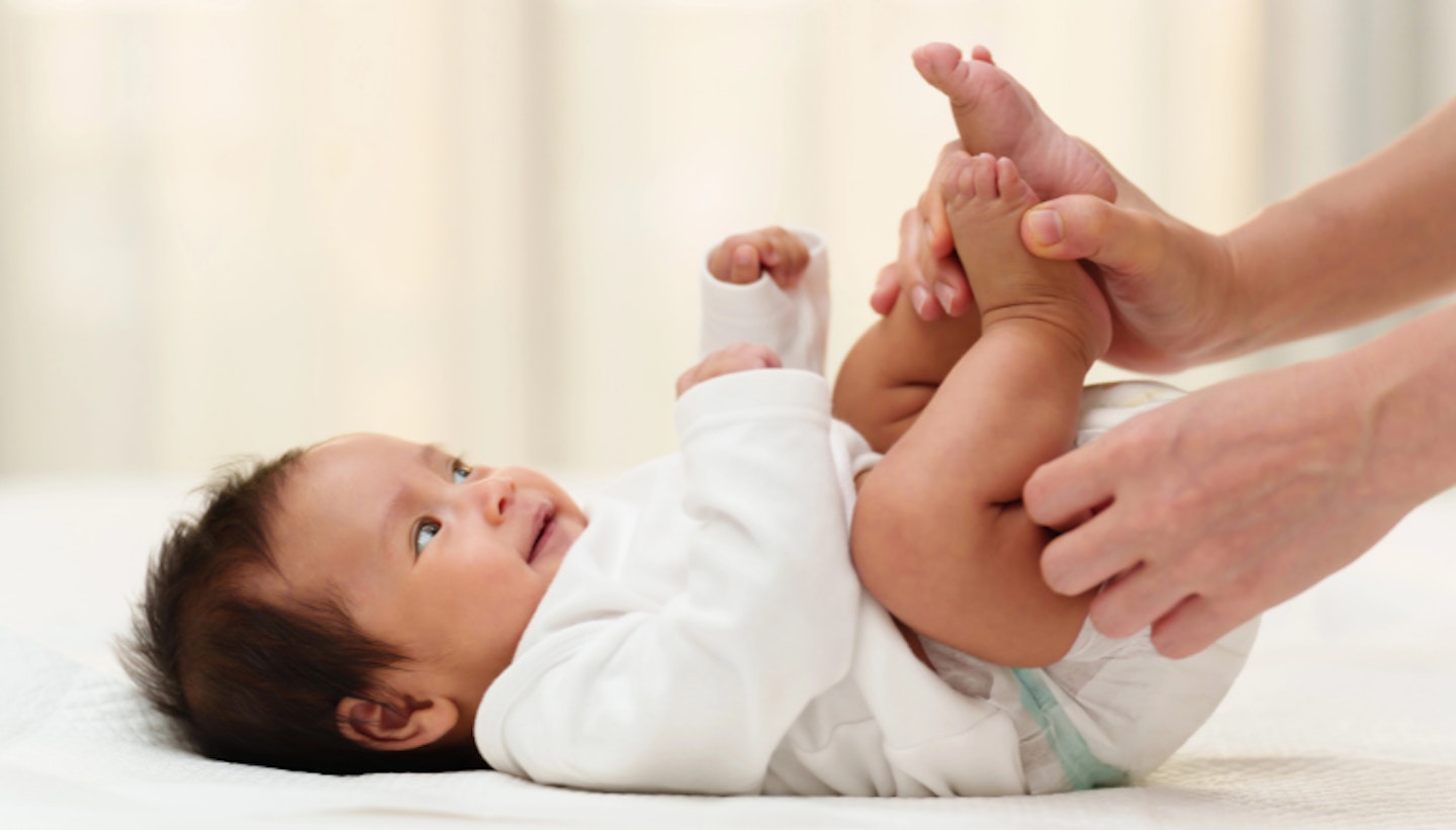 Mother changing diaper of newborn baby while lying on a bed