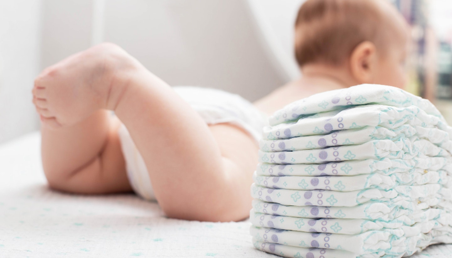 The legs of a baby in a diaper against the background of a stack of children's comfortable diapers.