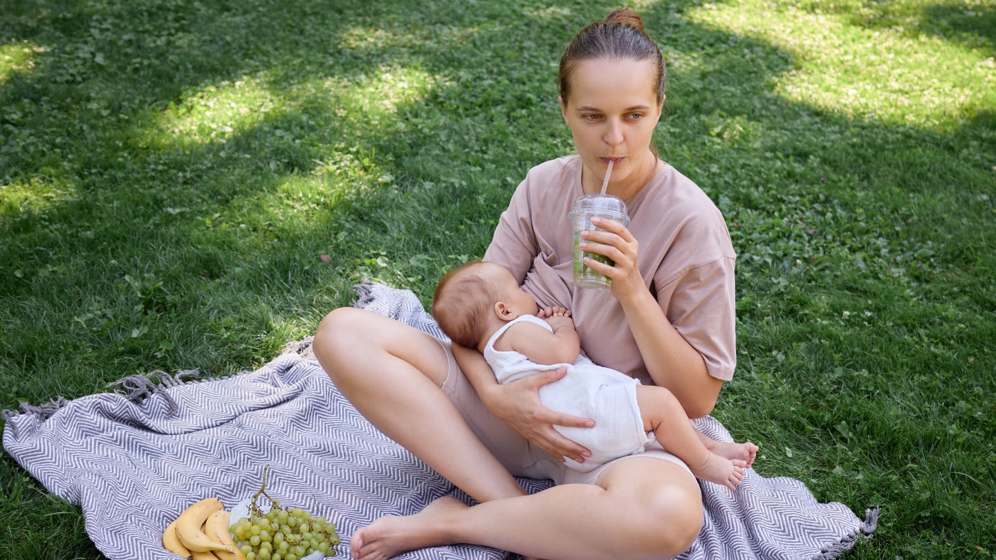 mother breastfeeding her baby under sun in park and drinking