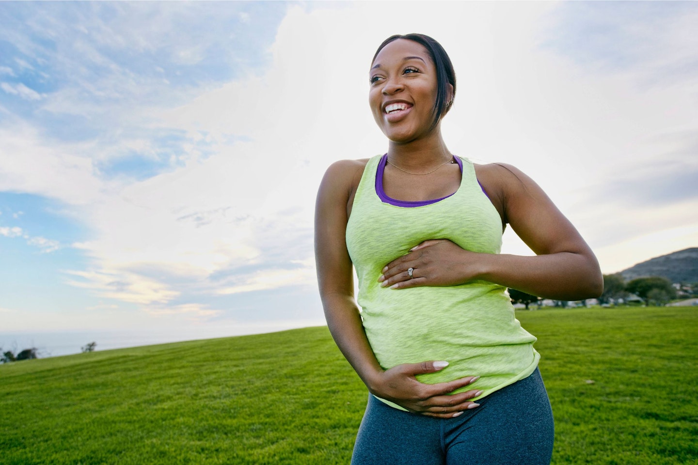 A pregnant black woman laughs while exercising in the park