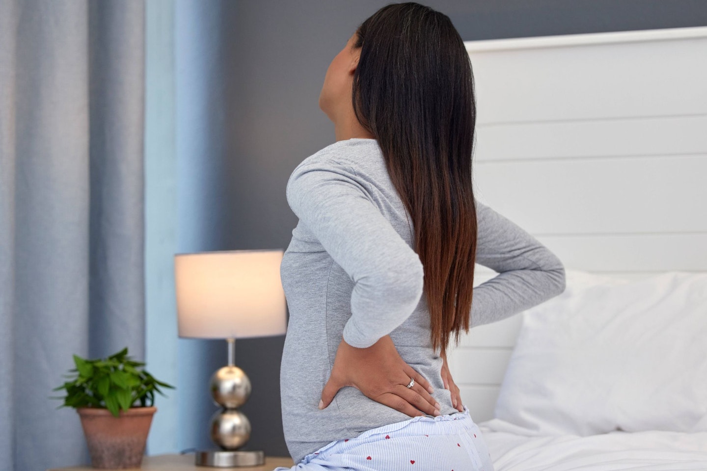 A pregnant person sits on their bed holding their lower back