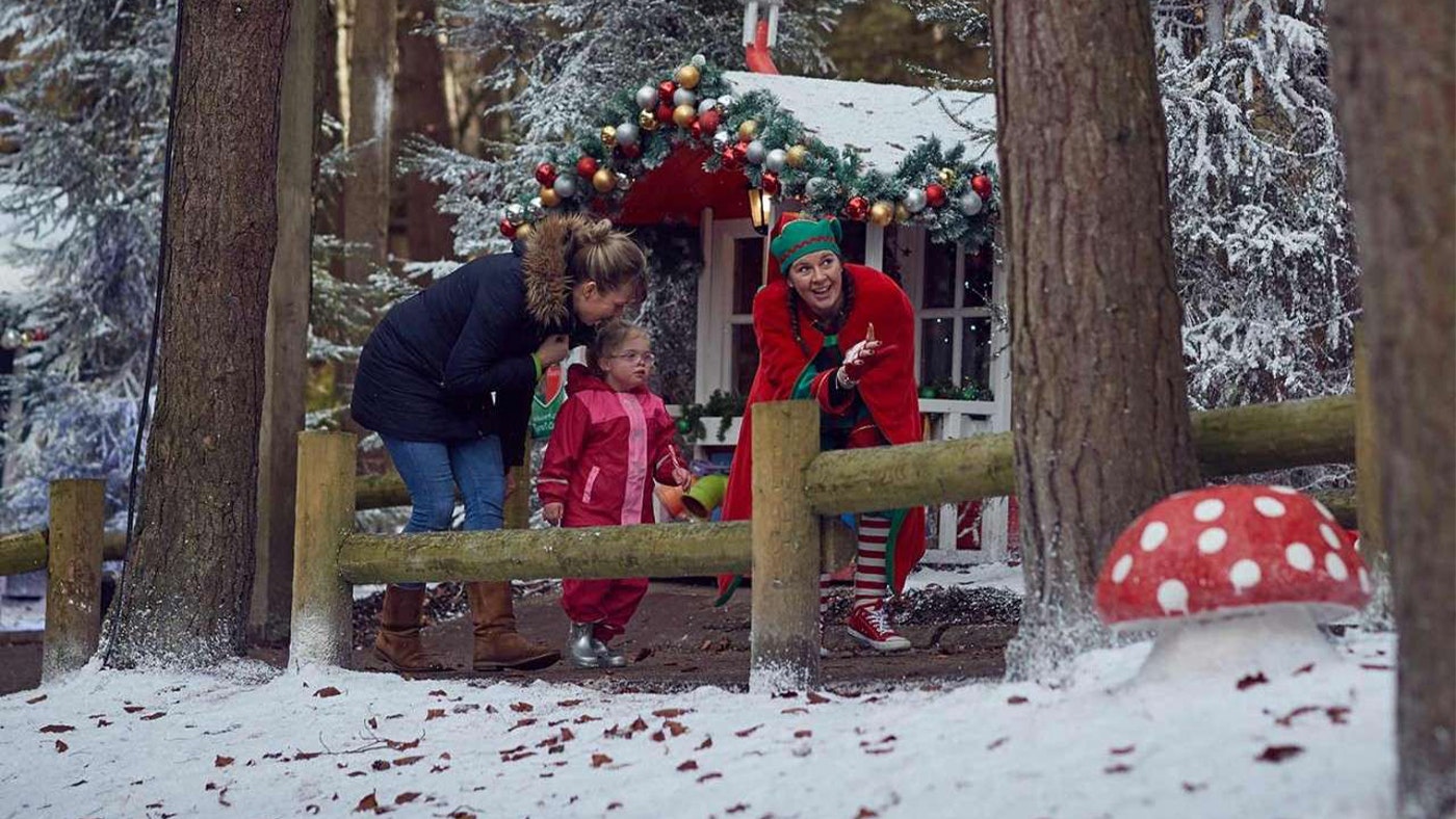 A little girl and her mum with an elf in front of a cabin in the woods at Centre Parcs